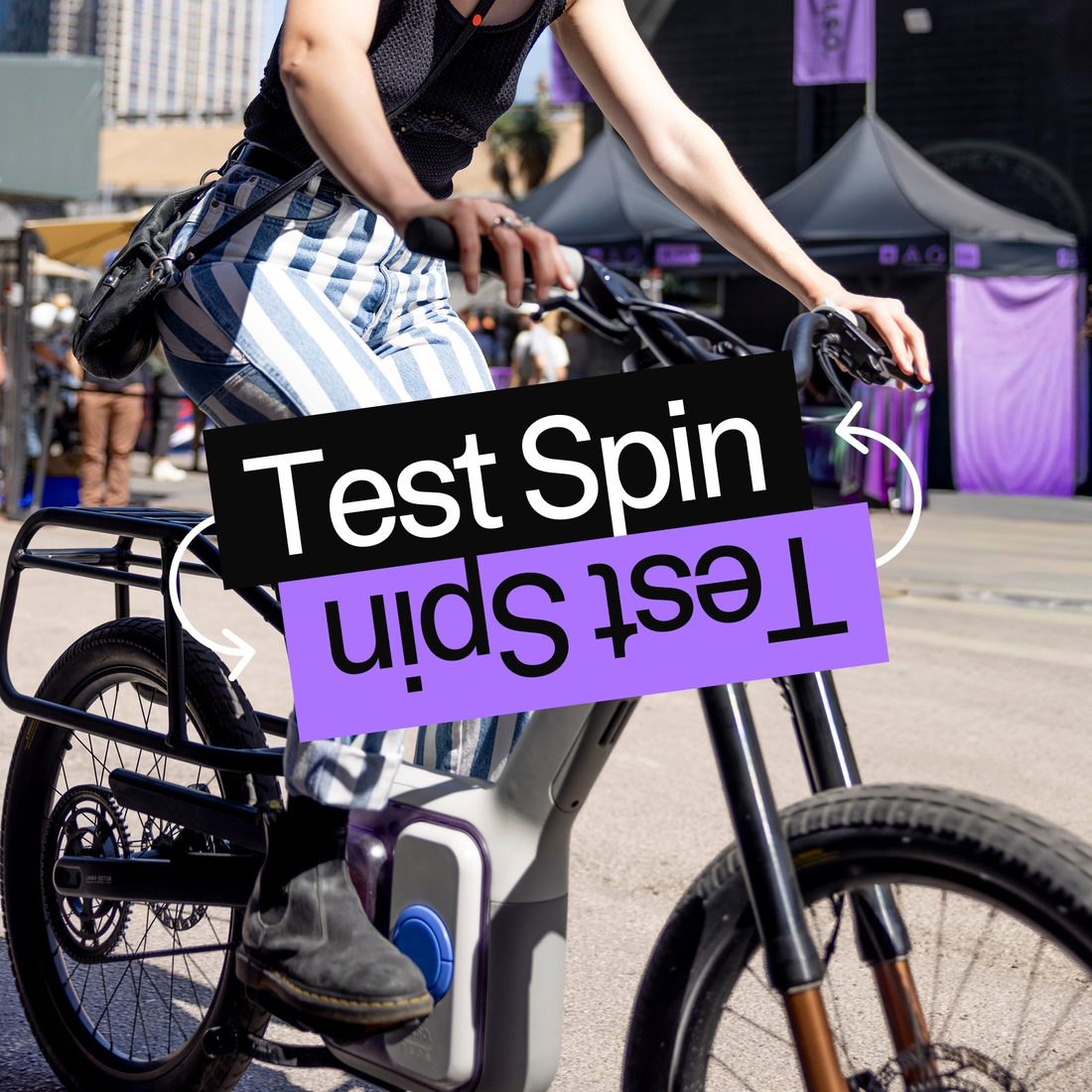 A rider swings onto a TM-B under an ALSO Test Spin sticker graphic at a city event.