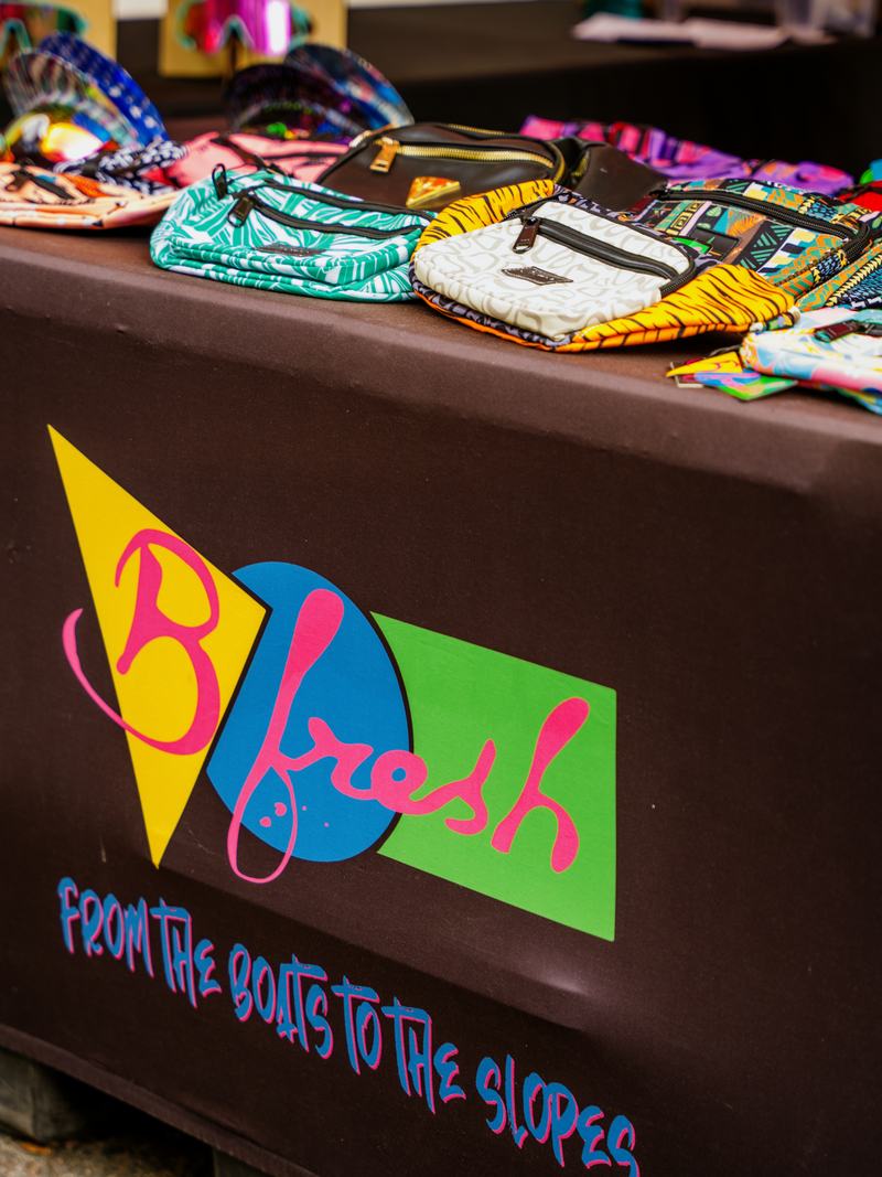 The neon B Fresh Gear booth with fanny packs, bucket hats, and visor sunglasses at a market.