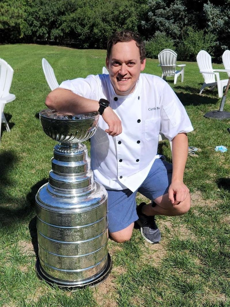 MisoHeat founder Chef Curtis Bell in a white chef's coat, kneeling beside the NHL Stanley Cup.