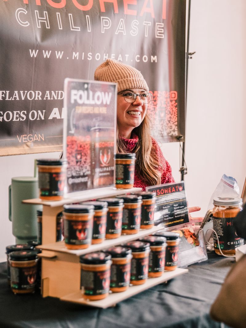 A pyramid display of MisoHeat chili paste jars at a market booth.