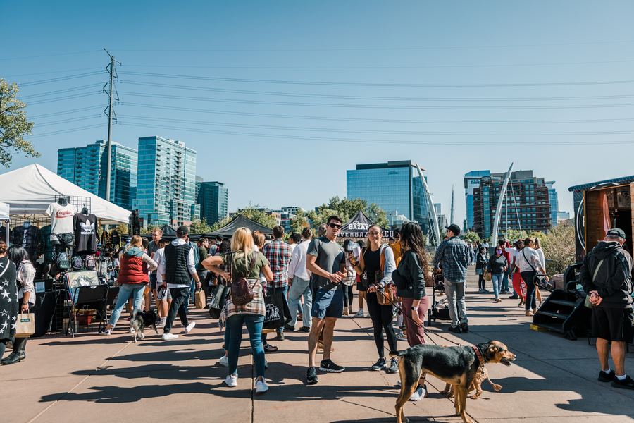 Crowds and dogs on the Commons Park plaza with the Denver skyline behind