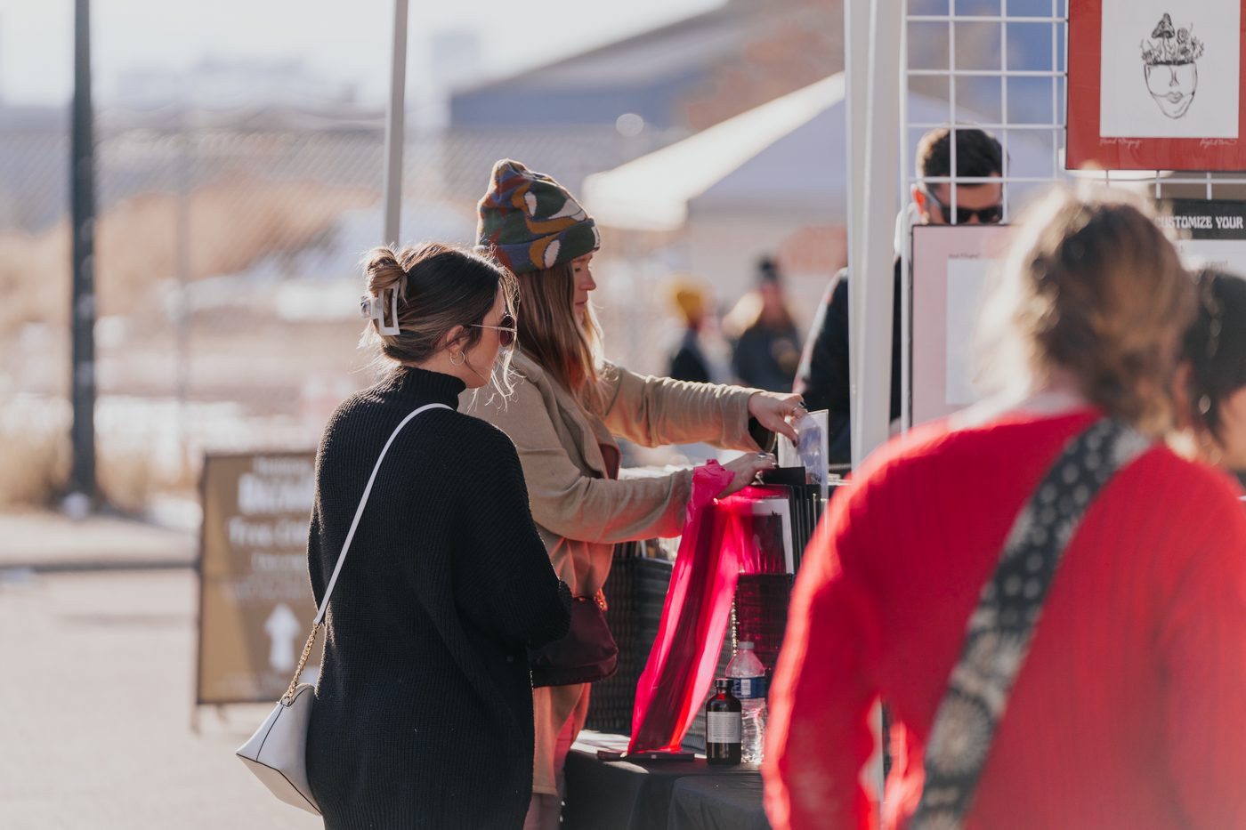 Shoppers browsing a maker booth strung with holiday lights at Holiday BAZAAR